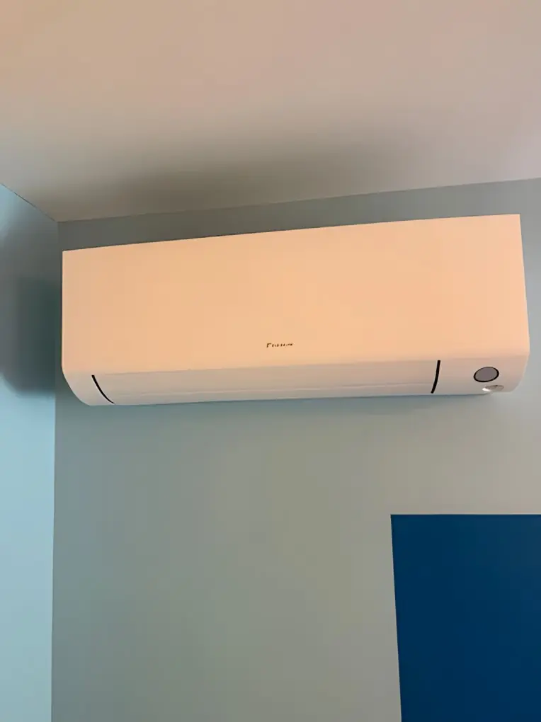 Climatiseur mural blanc posé sous le plafond d’une pièce aux murs bleu pâle, un pan bleu foncé en dessous
