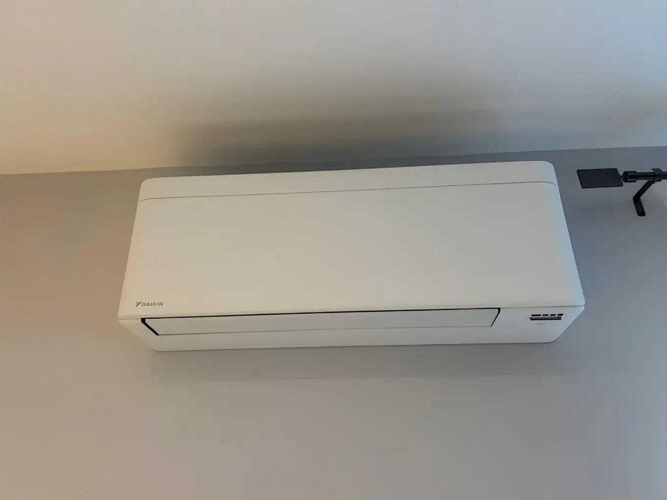 Climatiseur mural blanc vu de près et d’en dessous, volet de soufflage fermé, sur un mur beige